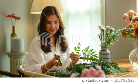 Pretty young woman small business owner preparing bouquet of pink flowers at tablet in her flower shop 103792585