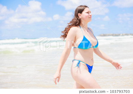 Slender beautiful girl walks on the white sandy beach of her hotel in a  bright trendy swimsuit, gently pulls her hand down her panties. Stock Photo