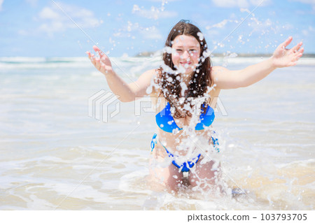 Sexy girl in a swimsuit splashing water towards the camera at the beach 103793705