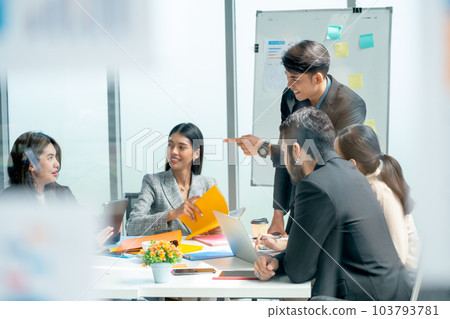 Asian business man present with whiteboard in front of meeting room and he also point to coworker Asian business man present with whiteboard in front of meeting room and he also point to coworker 103793781