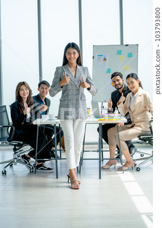 Asian pretty business woman stand in front of her co-workers sit in the back and she show thumbs up Asian pretty business woman stand in front of her co-workers sit in the back and she show thumbs up 103793800