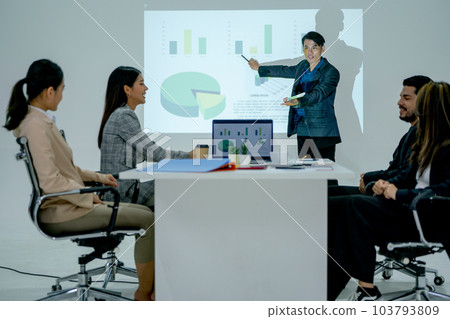 Pretty Asian business man stand in front of meeting room and present on white wall that projection 103793809