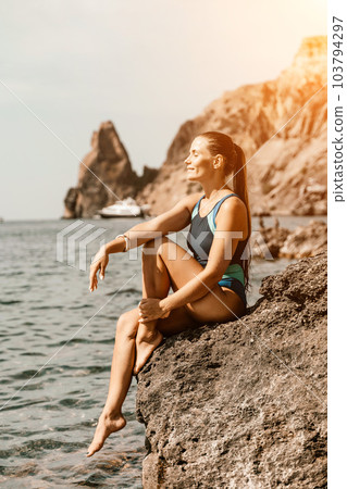 Woman travel summer sea. A happy tourist in a blue bikini enjoying the scenic view of the sea and volcanic mountains while taking pictures to capture the memories of her travel adventure. Woman travel summer sea. A happy tourist in a blue bikini enjoying the scenic view of the sea and volcanic mountains while taking pictures to capture the memories of her travel adventure. 103794297