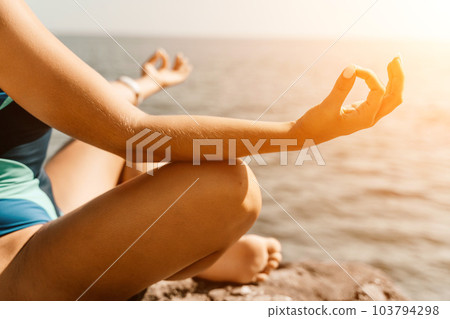 Yoga on the beach. A happy woman meditating in a yoga pose on the beach, surrounded by the ocean and rock mountains, promoting a healthy lifestyle outdoors in nature, and inspiring fitness concept. Yoga on the beach. A happy woman meditating in a yoga pose on the beach, surrounded by the ocean and rock mountains, promoting a healthy lifestyle outdoors in nature, and inspiring fitness concept. 103794298