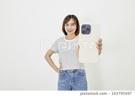 Young Asian female in t-shirt and blue jeans showing smartphone Young Asian female in t-shirt and blue jeans showing smartphone 103795097