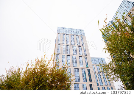 Blue beige modern apartment building, tree. Tile and glass facade. View from street, view from below 103797833