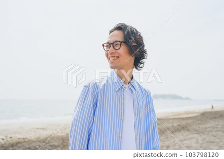 A man in a blue striped shirt walking along the beach A man in a blue striped shirt walking along the beach 103798120