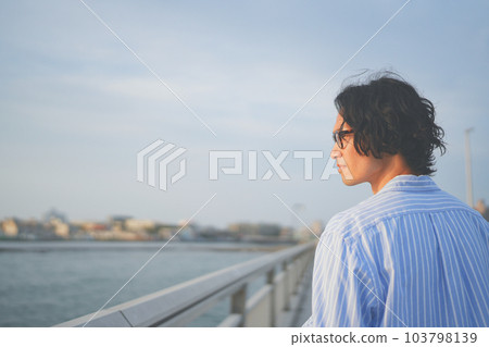 A man looking at the setting sun from a bridge A man looking at the setting sun from a bridge 103798139