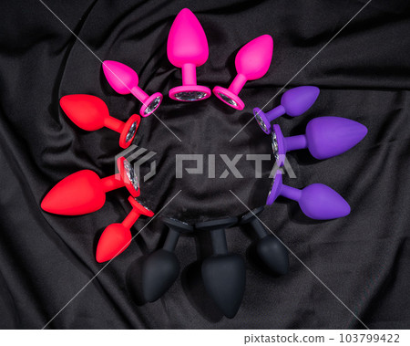 A set of silicone anal plugs in different colors and sizes on a black silk sheet.  103799422