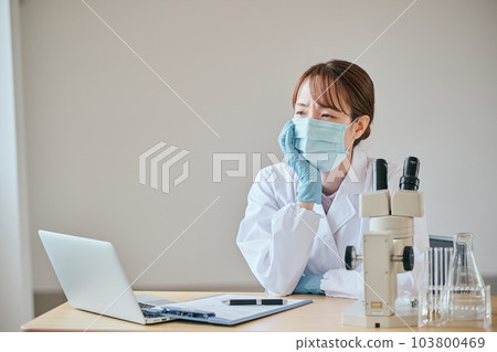 A young woman in a white coat with a melancholy expression at her desk 103800469