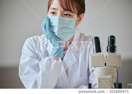 A young woman in a white coat with a melancholy expression at her desk 103800471