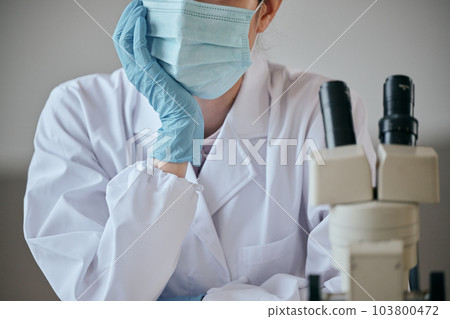 A young woman in a white coat with a melancholy expression at her desk 103800472