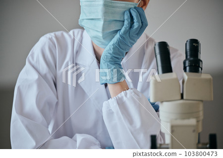A young woman in a white coat with a melancholy expression at her desk 103800473