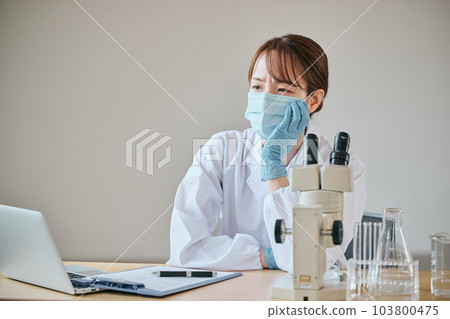 A young woman in a white coat with a melancholy expression at her desk 103800475
