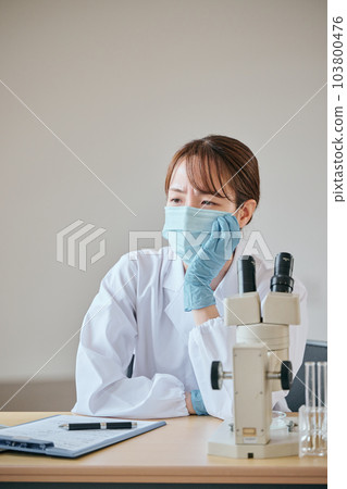 A young woman in a white coat with a melancholy expression at her desk 103800476