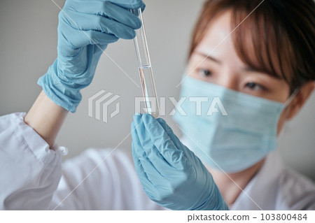 A young woman in a white coat doing an experiment 103800484