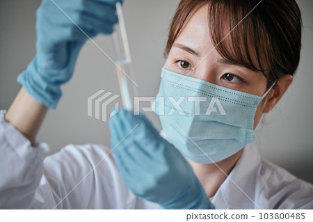 A young woman in a white coat doing an experiment 103800485