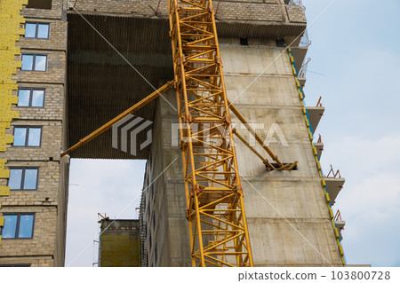 Attaching construction crane to building under construction. gray concrete center core of highrise building with yellow construction crane. Close-up Attaching construction crane to building under construction. gray concrete center core of highrise building with yellow construction crane. Close-up 103800728