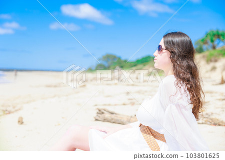 坐在沙灘上的白色衣服戴墨鏡的女孩 坐在沙灘上的白色衣服戴墨鏡的女孩 103801625