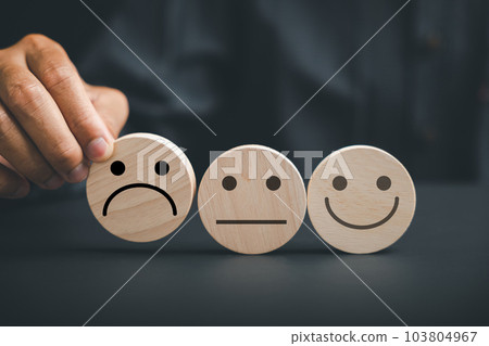Negative customer experience concept. Holding frown icon on wooden circle, customer expresses dissatisfaction and disappointment. Illustrating bad review, low score, and unsatisfied customer. Negative customer experience concept. Holding frown icon on wooden circle, customer expresses dissatisfaction and disappointment. Illustrating bad review, low score, and unsatisfied customer. 103804967
