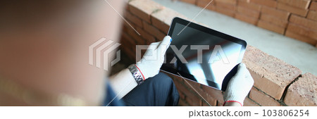 Builder stands in house under construction and holds tablet computer 103806254