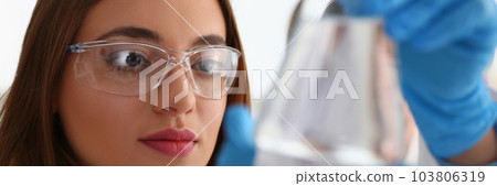 Portrait of woman scientist in glasses holds flask with transparent liquid Portrait of woman scientist in glasses holds flask with transparent liquid 103806319