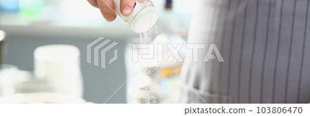 Cook pours salt into pan in kitchen 103806470