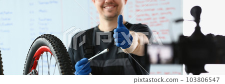 Male blogger holds thumbs up and repairs bicycle remotely Male blogger holds thumbs up and repairs bicycle remotely 103806547
