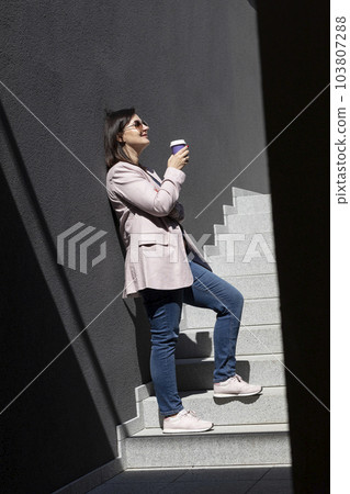 Beautiful Brunette Woman Drinks Coffee From Paper Cup, Standing On Stairs Near Office Outdoor, Dressed In Stylish Casual Clothes, Summer Sunny Day. Taking A Break. Lifestyle Mature Female. Vertical 103807288