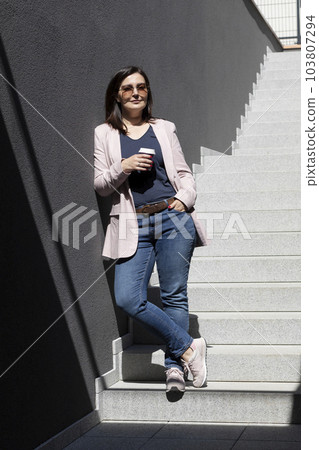 Smiling Beautiful Brunette Woman Hold Paper Cup Of Coffee Standing On Stairs Near Office Outdoor, Dressed In Stylish Casual Clothes, Summer Sunny Day. Taking A Break. Lifestyle Portrait Mature Female. Smiling Beautiful Brunette Woman Hold Paper Cup Of Coffee Standing On Stairs Near Office Outdoor, Dressed In Stylish Casual Clothes, Summer Sunny Day. Taking A Break. Lifestyle Portrait Mature Female. 103807294