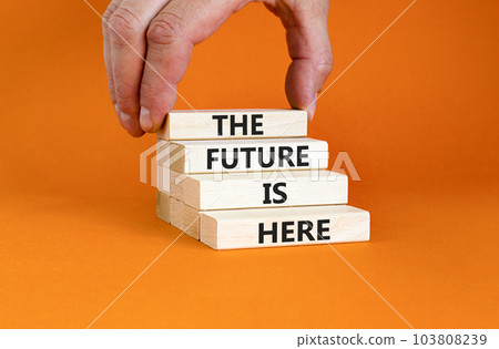 The future is here symbol. Concept words The future is here on wooden block. Beautiful orange table orange background. Businessman hand. Motivational business the future is here concept. Copy space. The future is here symbol. Concept words The future is here on wooden block. Beautiful orange table orange background. Businessman hand. Motivational business the future is here concept. Copy space. 103808239