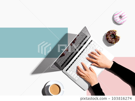 Person using a laptop computer with a donut and a cup of coffee 103816274