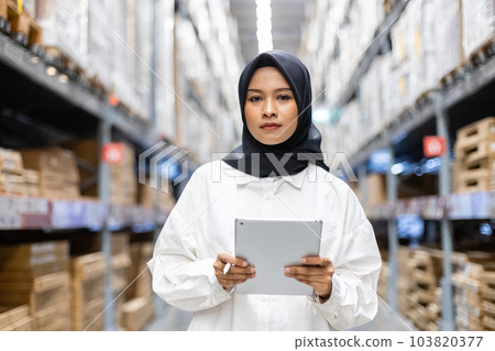 Portrait of Asian muslim female headscarf hijab holding digital tablet checklist product shelves. 103820377