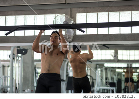 Strong athletic Asian young man pulling up on horizontal bar in gym Strong athletic Asian young man pulling up on horizontal bar in gym 103828123