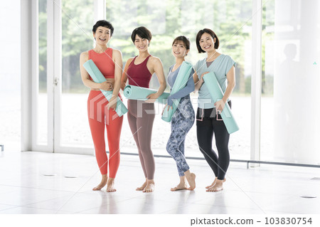 Portrait of four women holding yoga mats looking at the camera and smiling 103830754