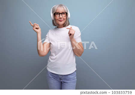 fashionable energetic woman 60s with gray hair listens to music in wireless headphones on studio 103833759