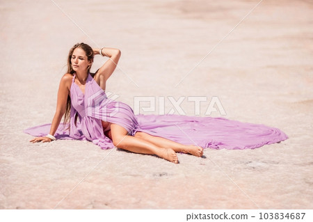 A woman in a pink dress sits on the salty shore of a pink lake and poses for a souvenir photo, creating lasting memories. 103834687