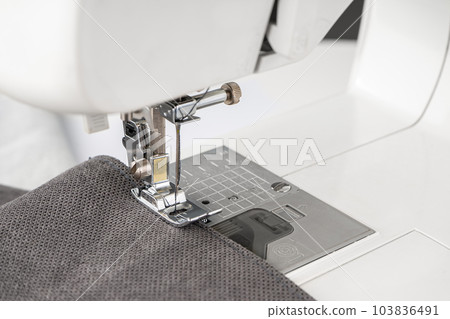 Modern sewing machine presser foot with gray fabric and thread, closeup Modern sewing machine presser foot with gray fabric and thread, closeup 103836491