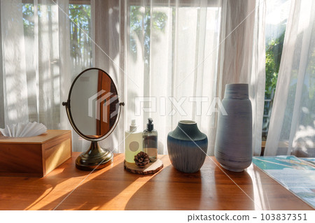 Dressing table with mirror, cream, vase and tissue box by white curtain 103837351
