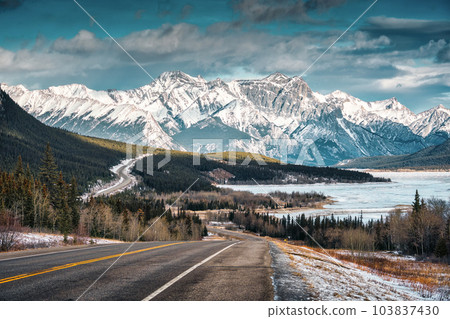 View of highway road into the rocky mountains and frozen lake in Icefields Parkway 103837430