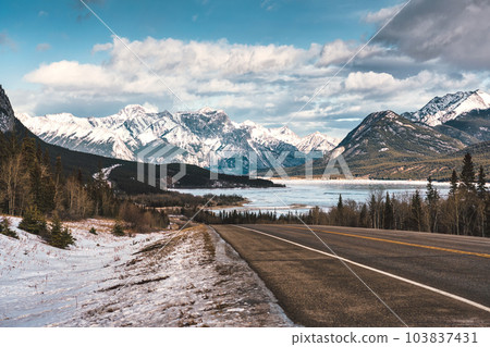 View of highway road into the rocky mountains and frozen lake in Icefields Parkway View of highway road into the rocky mountains and frozen lake in Icefields Parkway 103837431