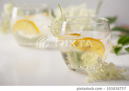 A cold drink made of elderflowers and lemon with ice on a light background A cold drink made of elderflowers and lemon with ice on a light background 103838757