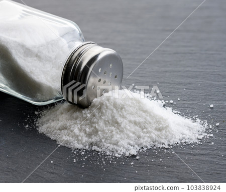 Salt glass jar and pile of spilled salt on a slate stone plate 103838924