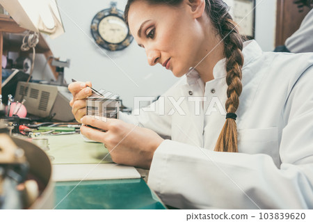 Woman watchmaker working diligently on repairing a watch 103839620