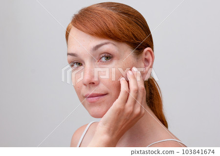 Portrait of cropped caucasian middle aged woman face with freckles touching skin by hand on white background looking at camera 103841674