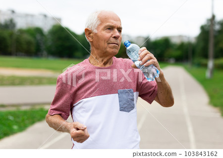 Old man with bottle of water standing outdoors 103843162