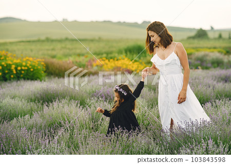 Mother with little daughter on lavender background. Beautiful woman and cute baby playing in meadow field. Family holiday in summer day. 103843598