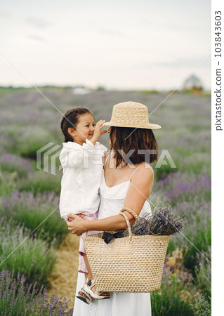 Mother with little daughter on lavender background. Beautiful woman and cute baby playing in meadow field. Family holiday in summer day. Mother with little daughter on lavender background. Beautiful woman and cute baby playing in meadow field. Family holiday in summer day. 103843603