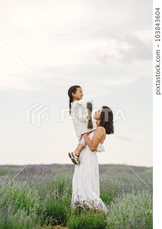 Mother with little daughter on lavender background. Beautiful woman and cute baby playing in meadow field. Family holiday in summer day. Mother with little daughter on lavender background. Beautiful woman and cute baby playing in meadow field. Family holiday in summer day. 103843604
