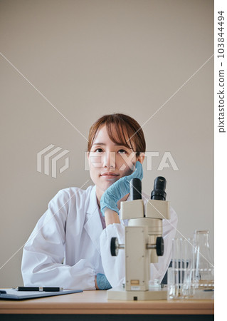 A young woman in a white coat thinking with her chin in her hands 103844494